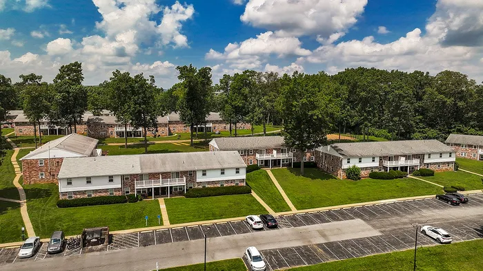 Charming apartment complex with brick buildings, lush green lawns, and ample parking under a vibrant blue sky.