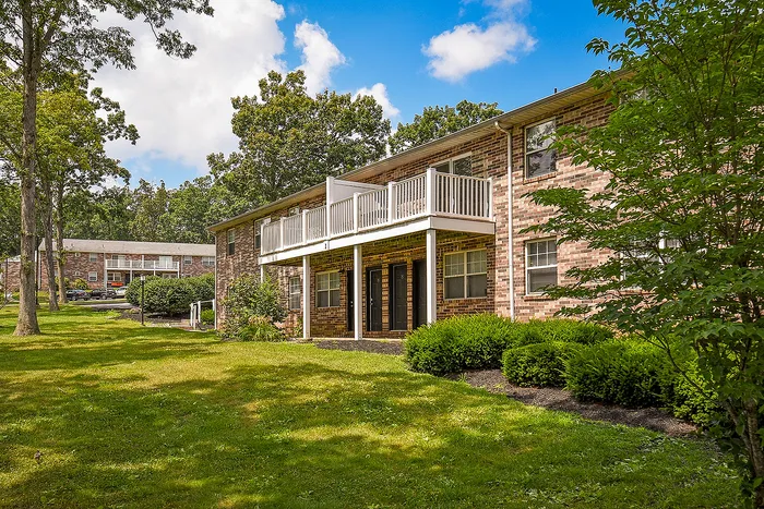 Charming brick apartment building with spacious balconies, set amidst lush green lawns and mature trees under a bright blue sky.