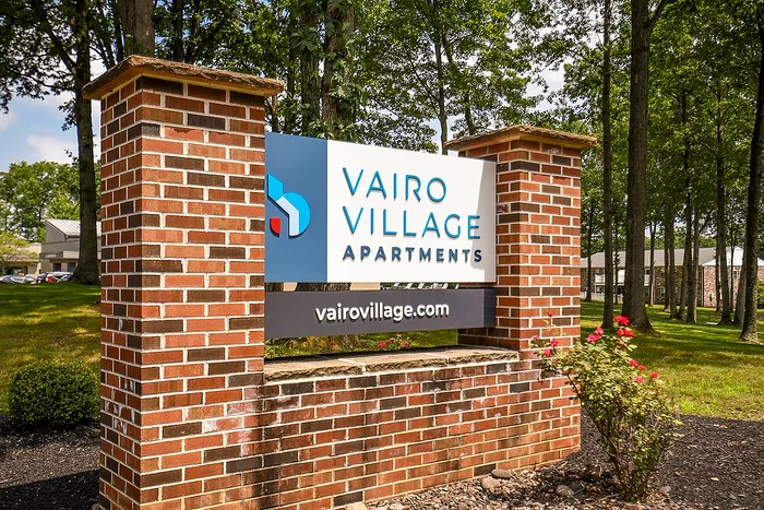 Inviting signage for Vairo Village Apartments surrounded by lush greenery and vibrant roses.