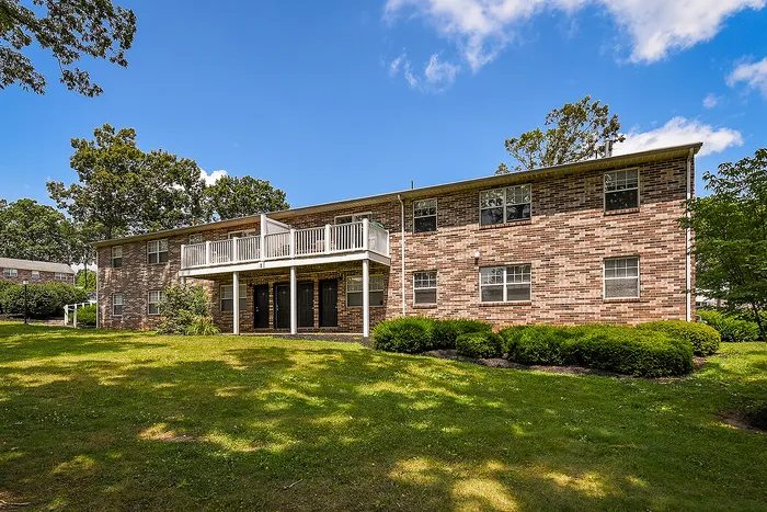 Charming brick apartment complex with spacious balconies set in a lush, green landscape on a sunny day.