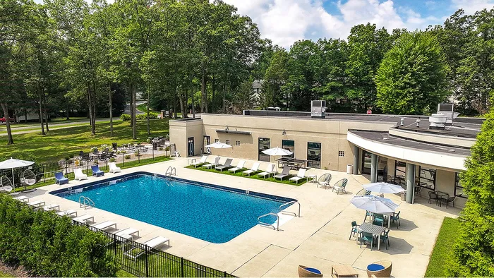 Charming outdoor pool area surrounded by lush greenery, featuring comfortable lounge chairs and shaded dining spaces for relaxation and enjoyment.