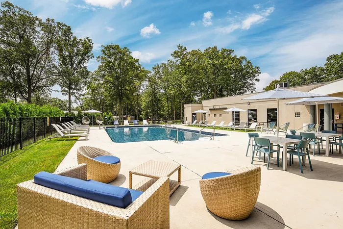 Inviting outdoor pool area surrounded by lush trees, featuring modern lounge chairs and stylish rattan seating, perfect for relaxation and summer enjoyment.