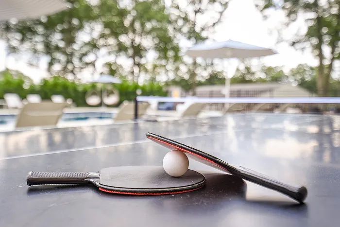 Inviting outdoor ping pong table beside a sunlit pool area, perfect for leisure and relaxation.