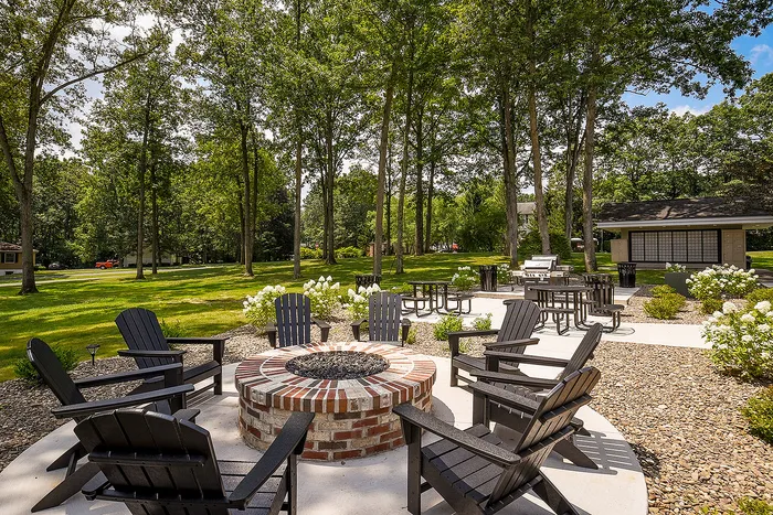 Inviting outdoor space with cozy firepit surrounded by Adirondack chairs, nestled among mature trees, perfect for gatherings and relaxation.