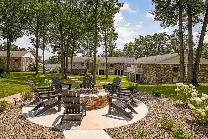 Inviting apartment complex featuring a serene outdoor seating area with cozy Adirondack chairs around a stylish fire pit, surrounded by lush greenery and vibrant gardens.