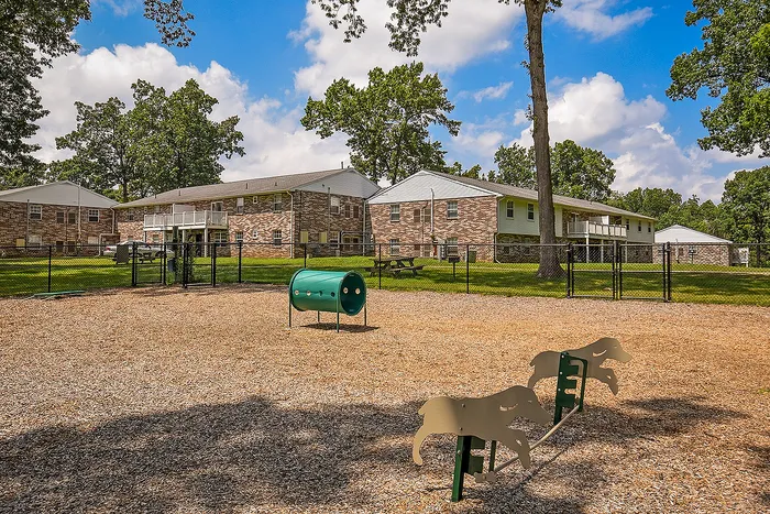 Charming residential complex with brick buildings and a playful outdoor space including a dog park, surrounded by lush greenery.