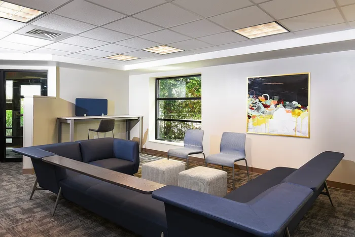 Modern lounge area featuring chic blue seating, a contemporary artwork, ample natural light, and sleek furniture for an inviting atmosphere.