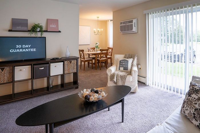 Inviting living space with modern decor, featuring a cozy armchair and dining area, accented by large windows and elegant shelving.