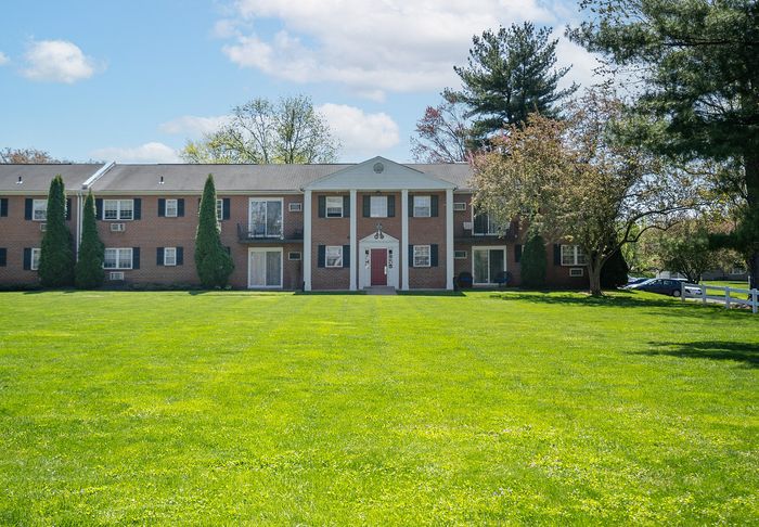 Charming brick apartment complex with elegant columns, set against a backdrop of lush green lawn and mature trees, perfect for serene living.