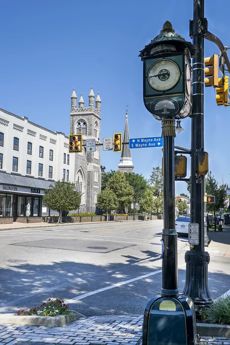 Charming urban scene featuring a historic clock tower and beautiful architecture, adjacent to tree-lined street with boutique shops.