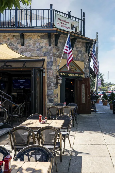 Charming stone facade of a lively pub with inviting outdoor seating and vibrant American flags, perfect for a sunny get-together.