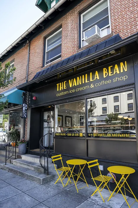 Charming cafe storefront of The Vanilla Bean, featuring bright yellow chairs and tables on a cozy sidewalk setting.