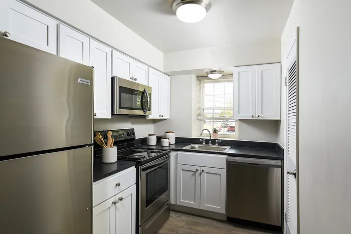 Modern kitchen with stainless steel appliances, sleek white cabinets, and a sunlit window over the sink.