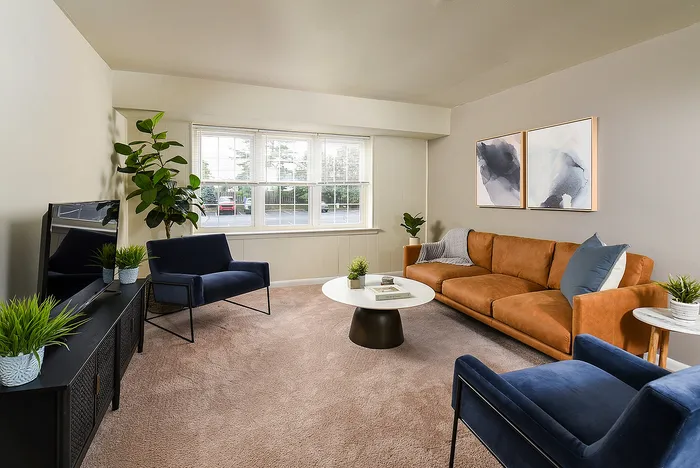 Inviting living room with contemporary decor, featuring a plush brown sofa, modern blue armchairs, and vibrant plants under abundant natural light.