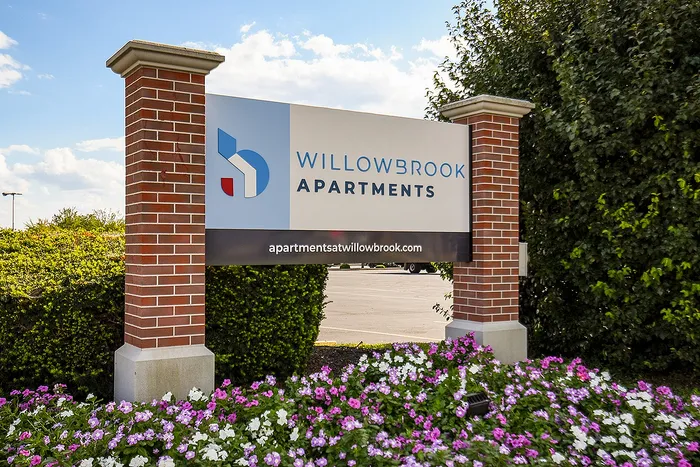Charming entry sign for Willowbrook Apartments surrounded by vibrant flower beds and lush greenery.