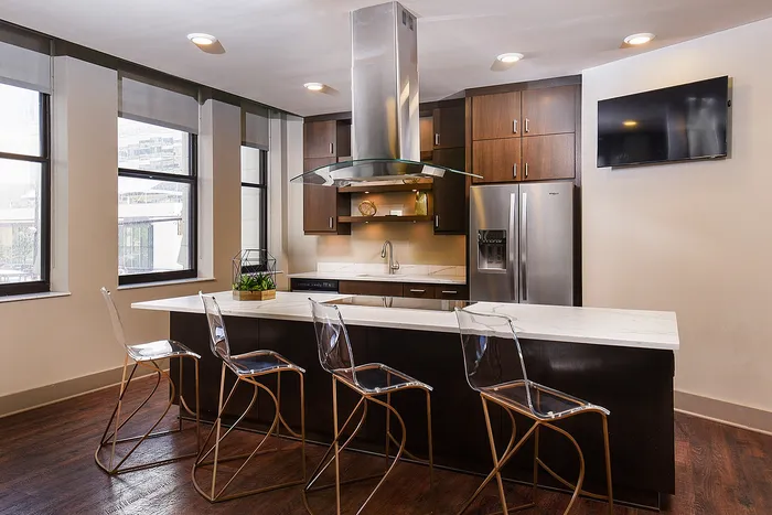 Modern kitchen with sleek dark wood cabinets, stainless steel appliances, and a stylish marble island with transparent bar stools.