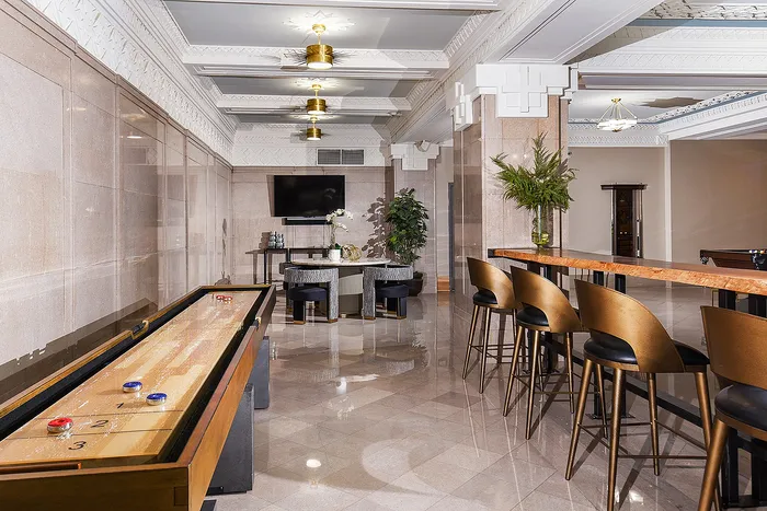 Luxurious game room featuring sleek bar stools, a shuffleboard table, and elegant decor with modern lighting.
