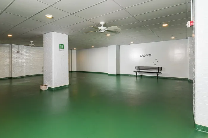 Spacious indoor area with sleek green flooring, modern ceiling fans, and a minimalist bench, perfect for versatile communal use.