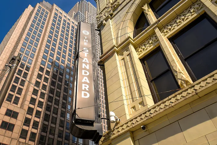 Impressive view of The Standard building's elegant facade against a backdrop of towering architecture, showcasing urban sophistication and architectural grandeur.