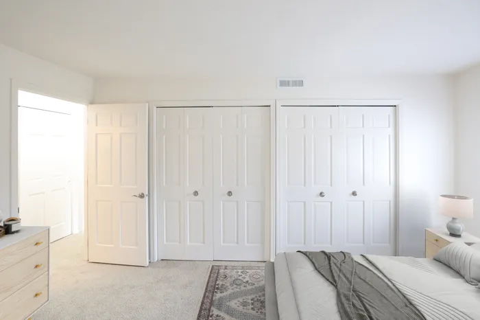 Bright and airy bedroom with elegant white wardrobes, a cozy bed, and soft carpeting creating a serene atmosphere.