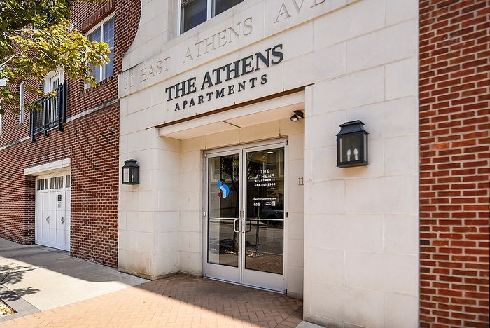 Charming entrance of The Athens Apartments featuring elegant brick facade and inviting glass doors.