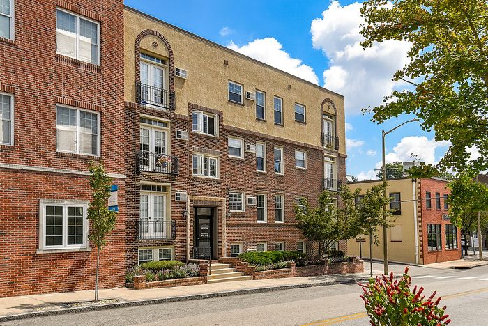 Charming multi-level apartment building with classic brick facade and elegant balconies, set against a bright blue sky.