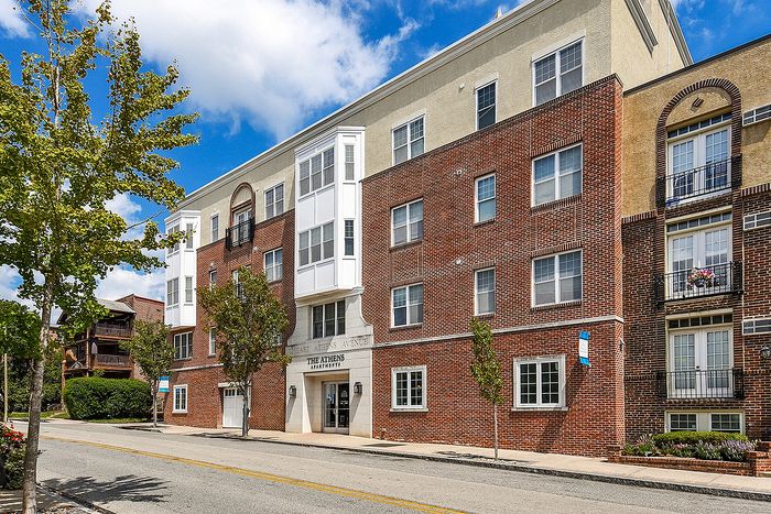 Charming red-brick apartment building with modern white accents, set against a clear blue sky, offering urban living with natural street-side greenery.