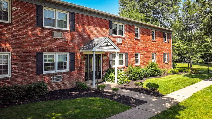 Charming two-story red brick apartment with classic architecture, surrounded by lush greenery and manicured lawns.