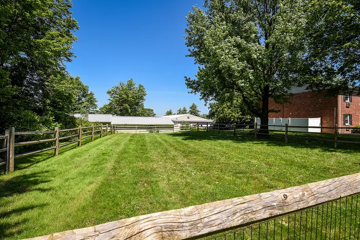 Charming residential property featuring a lush green yard, sturdy wooden fencing, and mature trees under a clear blue sky.