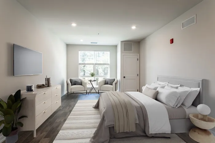 Cozy bedroom with a modern design featuring a plush bed, soft lighting, and stylish armchairs by a window inviting natural light.
