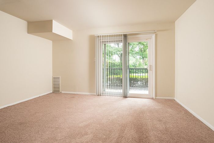 Bright living room with plush carpet flooring, expansive windows, and a view of lush greenery, perfect for relaxation.