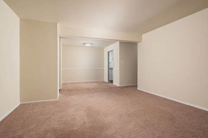 Charming apartment featuring a spacious carpeted living area with soft beige walls and stylish lighting, perfect for cozy living.