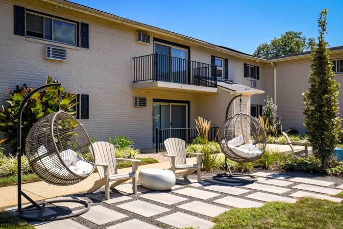 Inviting apartment exterior with modern balconies, stylish egg chairs, and lush landscaping, perfect for relaxation.