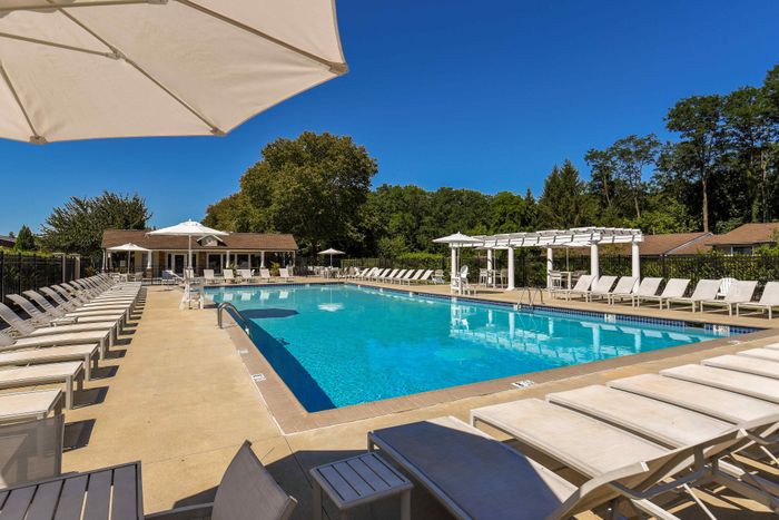 Luxurious outdoor pool area with crisp blue water, surrounded by elegant lounge chairs and shaded umbrellas, set against a backdrop of lush greenery.