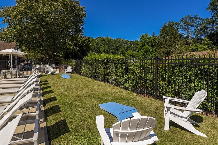 Inviting outdoor recreational space featuring cornhole boards, lounge chairs, and vibrant greenery under a bright blue sky.