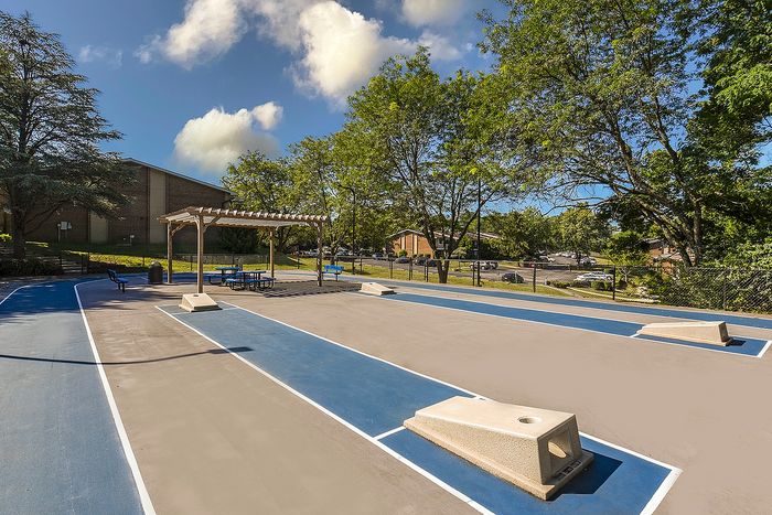 Inviting outdoor recreation area featuring a spacious court, shaded seating under a pergola, and lush greenery in a serene community setting.