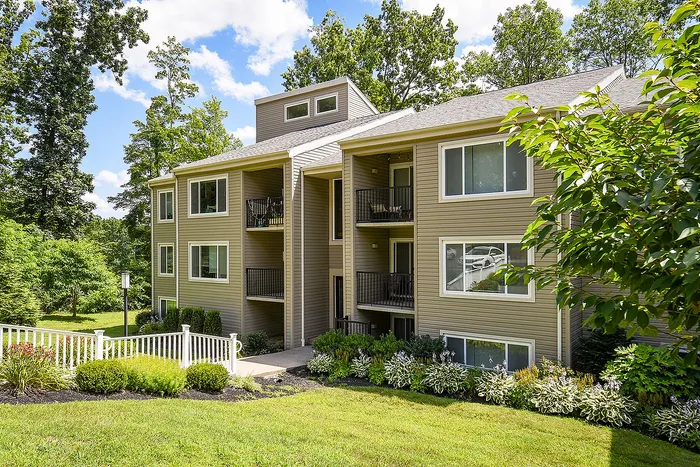 Charming apartment exterior with modern design, surrounded by lush greenery and bright landscaping, under a clear blue sky.
