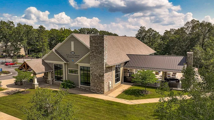 Charming club and leasing center nestled in lush greenery with stone accents and large glass windows, offering a serene and inviting entrance.