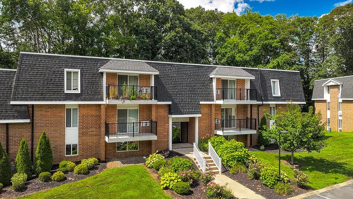Charming brick apartment complex with modern balconies, lush landscaping, and surrounded by serene greenery.