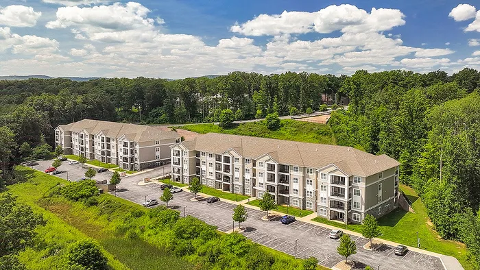 Charming aerial view of a modern apartment complex surrounded by lush greenery and scenic landscapes, offering serene living with ample parking and close proximity to nature.