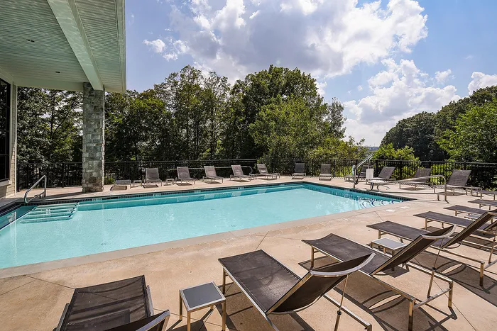 Inviting outdoor pool with sleek lounge chairs, surrounded by lush greenery and a serene forest backdrop.