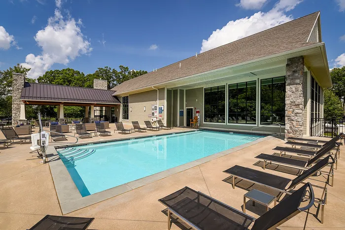Inviting apartment community pool area with sun loungers, surrounded by lush trees and modern architectural design.