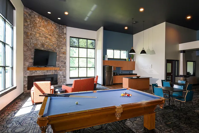 Elegant recreation room with a pool table, cozy seating area, modern kitchenette, and large windows overlooking greenery.
