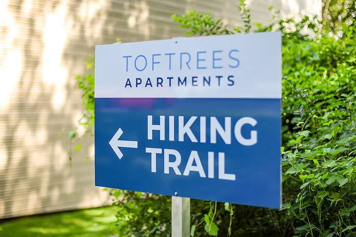 Inviting trail sign at Toftrees Apartments, promising scenic hiking adventures in lush greenery.