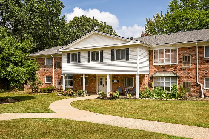 Charming two-story apartment building with a classic brick facade, surrounded by lush greenery and a welcoming walkway.