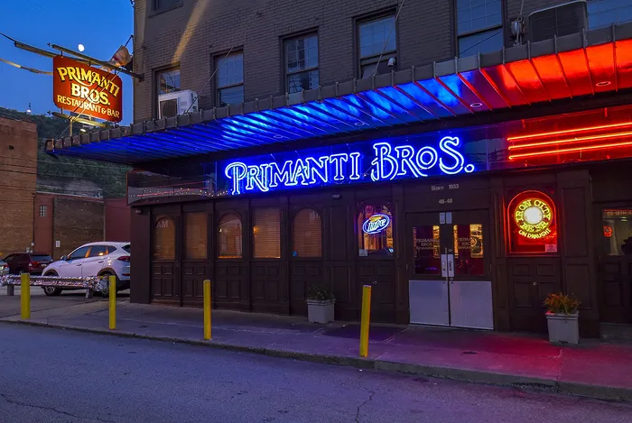 Vibrant evening view of Primanti Bros. restaurant and bar with striking neon signage illuminating the exterior.