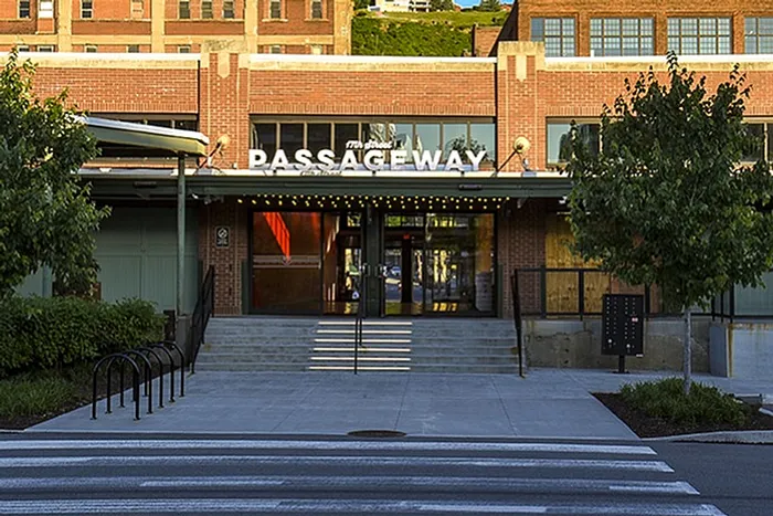 Inviting entrance with a striking red brick facade, lush greenery, and a modern crosswalk leading to an elegant building labeled 'Passageway'.