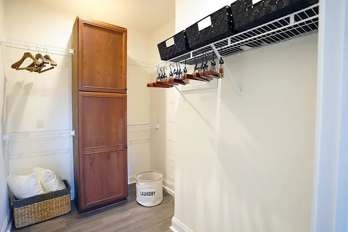 Elegant walk-in closet with ample space, featuring wooden cabinetry, organized shelving, and laundry basket.