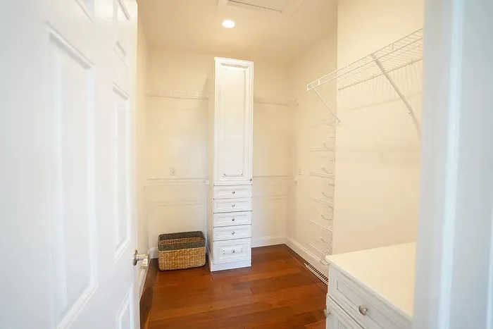 Elegant walk-in closet with ample shelving, warm hardwood floors, and a central cabinet offering stylish storage solutions.