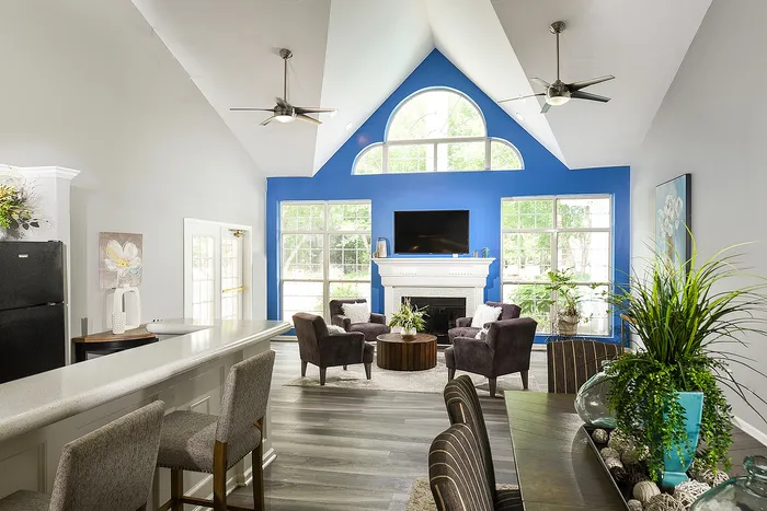 Elegant resident lounge with vaulted ceiling, vibrant blue accent wall, cozy seating around a chic coffee table, and large windows flooding the space with natural light.